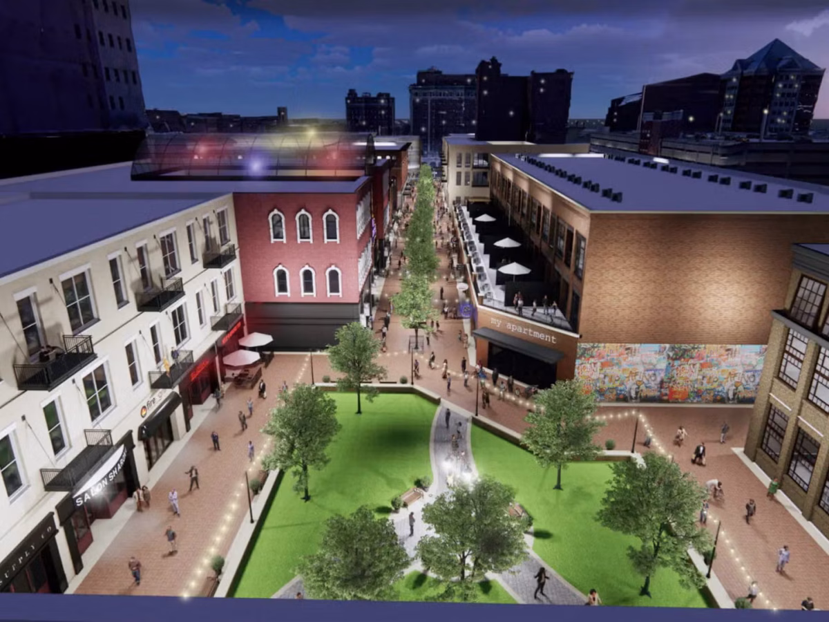 A rendering shows an open-air plaza surrounded by buildings, with a green area in the center with trees and walking paths.