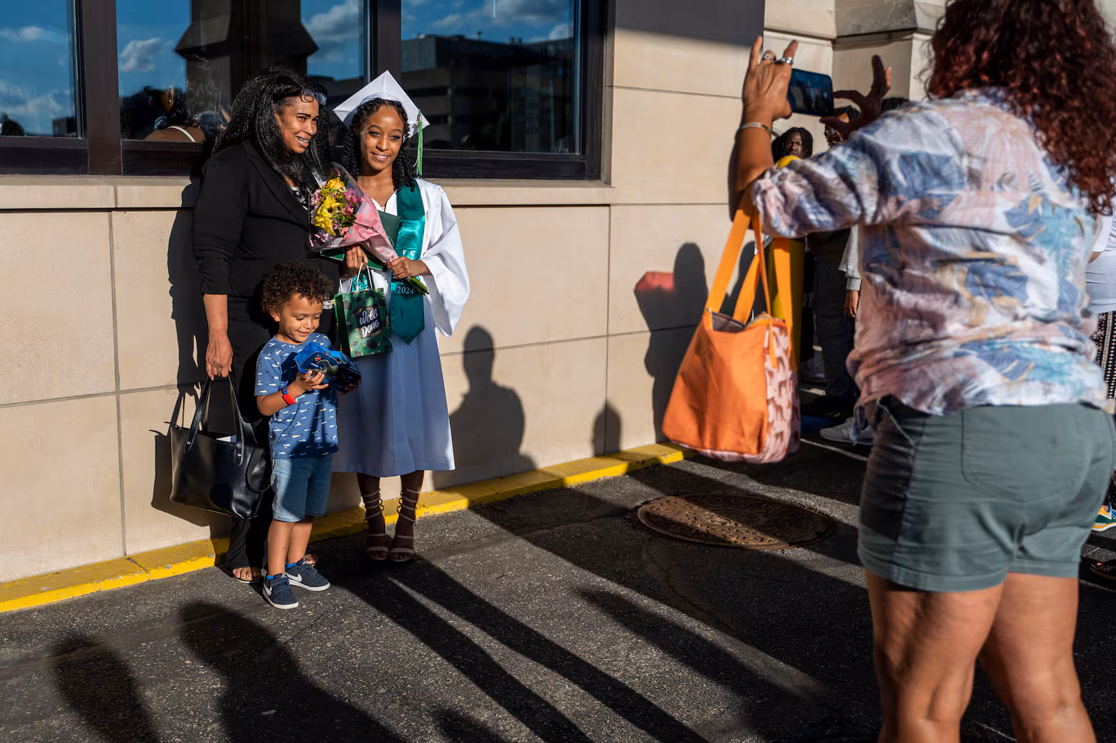 A high school student wearing a white graduation gown poses for a photo with her vamily on a sunny day.